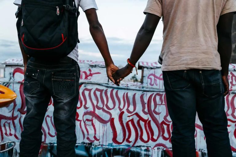 A photo taken from behind two men who are holding hands.