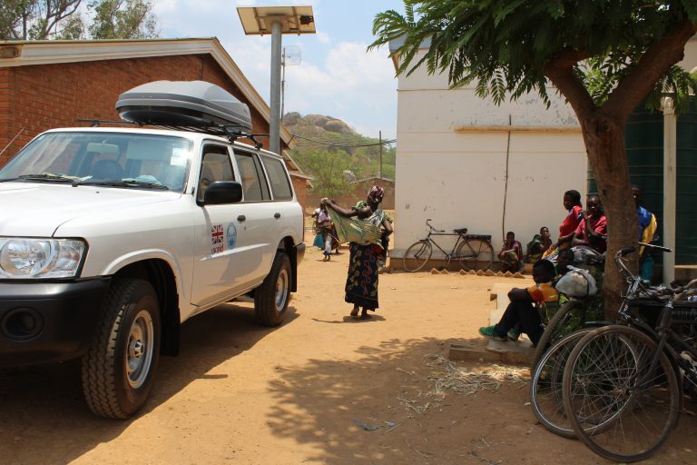 A large white car is parked outside of a health clinic.