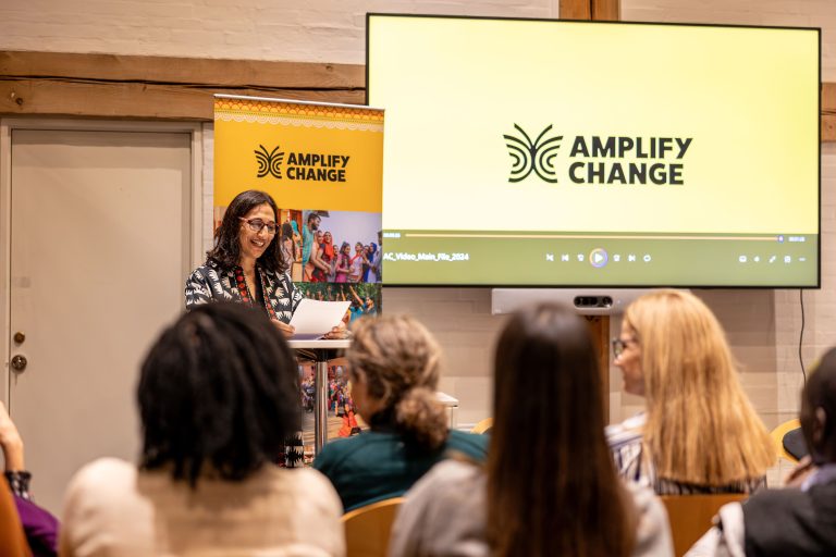 A woman stands at a podium at the front of a room smiling